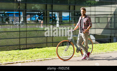 Hübscher junger Mann mit dem Fahrrad in einer Gasse vor einem Glasgebäude Stockfoto