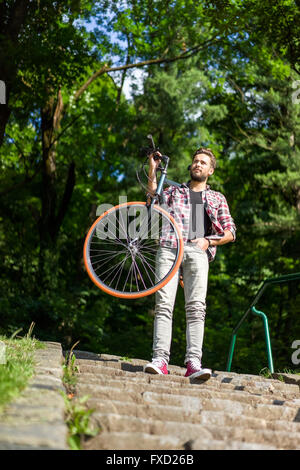 ein mächtiger Mann sein Motorrad auf der Schulter hängend auf Treppe, Blick weit entfernt bleiben. Stockfoto