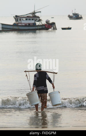 Wasser Träger Frau & Boote in der Morgendämmerung, Strand in Danang, Vietnam Stockfoto