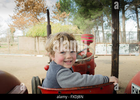 Lächelnd drei Jahre alten Jungen auf der Suche über die Schulter auf roten Oldtimer-Traktor Stockfoto