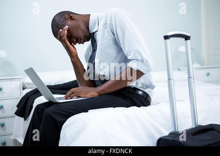 Gespannten Mann am Bett sitzen und mit laptop Stockfoto