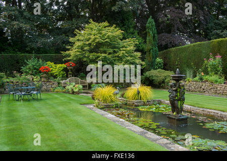 Einen privaten, traditionellen, gepflegten, ländlichen Garten, West Yorkshire, England - Teich, Brunnen und Liegewiese im Sommer. Stockfoto