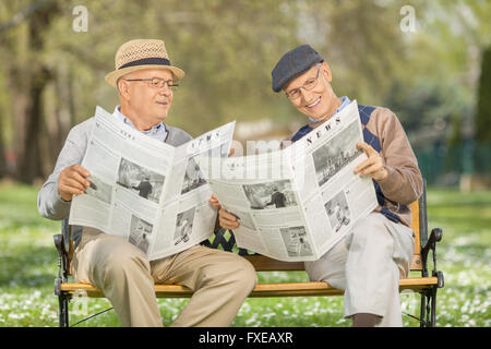 Ältere Gentleman zeigt etwas in der Zeitung zu einem Freund sitzt auf einer Holzbank in einem park Stockfoto