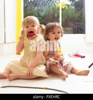 Zwei Kleinkinder Mädchen sitzen auf Boden essen Eis am Stiehl Stockfoto