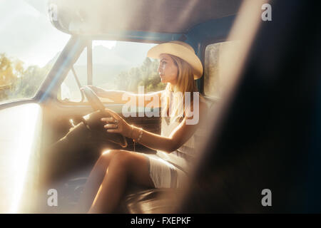 Porträt der schönen jungen Frau, die einen Hut Autofahren auf sonnigen Tag. Junges Mädchen auf einem Roadtrip. Stockfoto