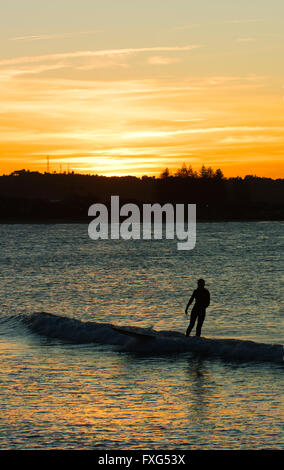 Surfer reitet eine kleine Welle auf dem Pass bei Sonnenuntergang. Stockfoto