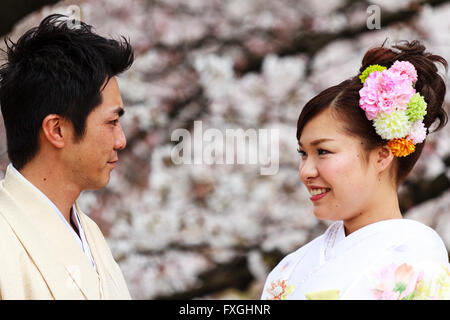 Japanische junges Paar. Mann und Frau, Braut und Bräutigam. Kopf und Schultern, einander zugewandt, beide lächelnd, glücklich. Kirschblüten hinter Ihnen. Stockfoto