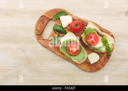 Offenen Sandwiches gemacht von Ciabatta, getrockneten Tomaten, cremiger Käse und Salat Blatt Basilikum auf einem hölzernen Cutboard. Antipasti Stockfoto