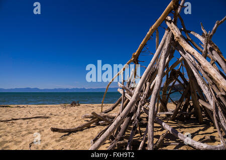 Abel Tasman NP, NEW ZEALAND im Februar 2016: ein Zelt aus Zweigen gemacht steht an einem leeren Strand. Der Himmel ist blau und die Sonne ist Stockfoto