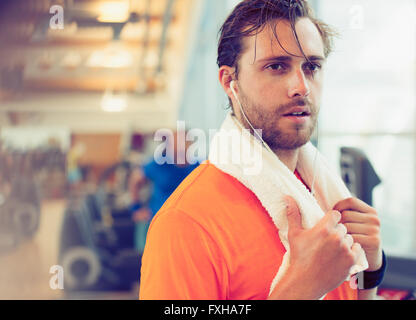 Mann mit Handtuch und Kopfhörer ruhen im Fitnessstudio schwitzen Stockfoto