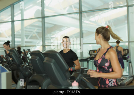Lächelnde Frauen reden und Joggen auf dem Laufband im Fitnessstudio Stockfoto