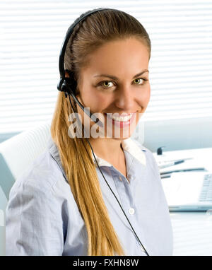 Einzelne glücklich schöne Frau mit langen Pferdeschwanz mit Telefon Kopfhörer im Call-Center oder im kleinen Büro mit Jalousien im Hintergrund Stockfoto