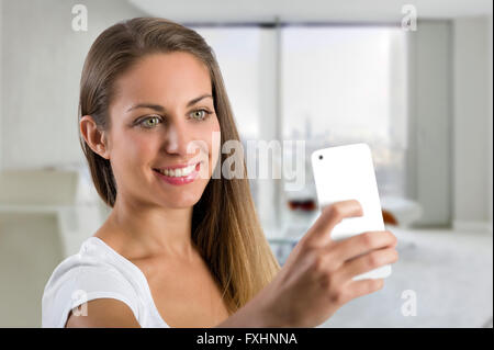 Einzelne süß lächelnde Frau nimmt ein Selbstporträt im Büro mit Smartphone-Kamera in der hand in der Nähe von ihrem Gesicht Stockfoto
