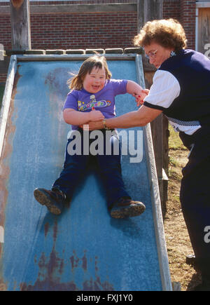 Lehrerin hilft behinderten Schüler auf die sliding board Stockfoto