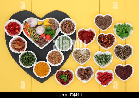 Kräutern und Gewürzen Zutaten auf ein Herz geformt Schiefer und Porzellan Geschirr aus Holz gelb hinterlegt. Stockfoto