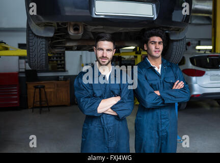 Mechanik mit Arme gekreuzt vor einem angehobenen Fahrzeug steht Stockfoto