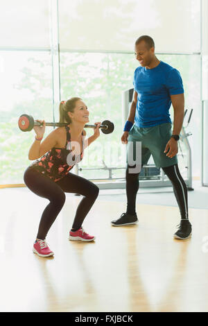 Persönlicher Trainer führt Frau macht Kniebeugen im Fitnessstudio Stockfoto