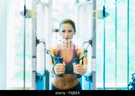 Fokussierte Frau mit Kabel Trainingsgeräten im Fitnessstudio