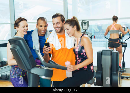 Lächelnden Freunde mit Handy am Heimtrainer im Fitness-Studio Stockfoto