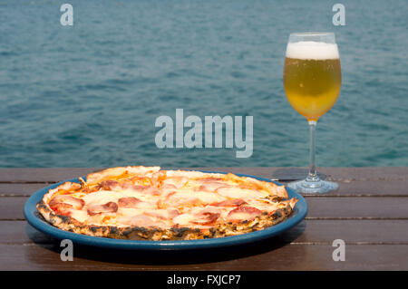 Frische Peperoni-Pizza auf einen blauen Teller und Glas Bier auf Holz und Wasser-Hintergrund Stockfoto