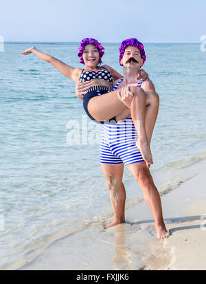 Mann im Badeanzug mit in seine Arme eine Frau im Badeanzug am Meeresstrand Stockfoto