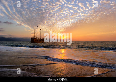 Piratenschiff ist eine alte hölzerne Piratenschiff mit voller Fahnen in einem farbenfrohen Sonnenuntergang Himmel nach Sonnenuntergang am Meer Horizont. Stockfoto