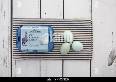 Alten Cotswold erscheinen freien Bereich Eiern mit Pastell farbigen Schalen in einer Box auf einer blau-weiß gestreiften Serviette über rustikalen Tisch Stockfoto
