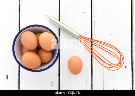 Eiern in einer Keramikschale mit einem Schneebesen auf einem rustikalen weiß lackierten Holztisch von oben geschossen Stockfoto
