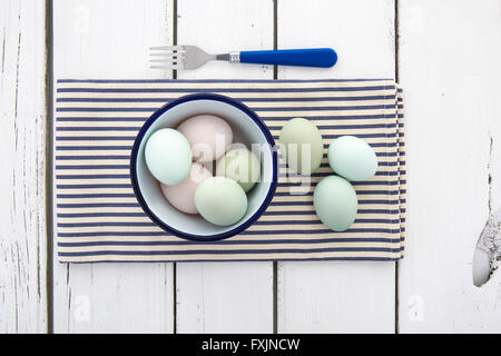 Alten Cotswold erscheinen freien Bereich Eiern mit Pastell farbigen Schalen in einer Schüssel auf einer blau-weiß gestreiften Serviette über rustikalen Tisch Stockfoto