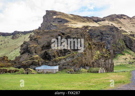 Vulkangestein Berg mit Rasen Häuser auf Ackerland in Island Stockfoto