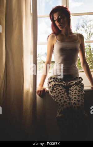 Schöne junge Frau sitzt auf der Fensterbank Stockfoto