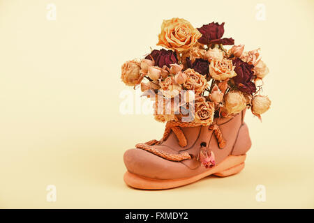 Getrocknete rote und gelbe Rosen Blumenstrauß in kleine keramische Schuh auf zartes gelbes Papierhintergrund Stockfoto