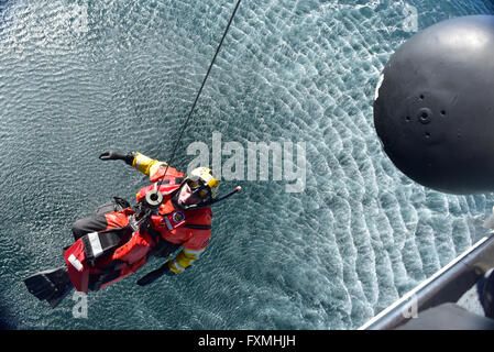 Ein uns Küstenwache Rettung Schwimmer ist aus dem Wasser in einem MH-60 Jayhawk Helikopter während Rettung Ausbildung im Pazifischen Ozean 12. Januar 2016 in der Nähe von San Diego, Kalifornien gehisst. Stockfoto