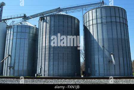 Drei Metallsilos an einem klaren Tag vor Eisenbahnschienen. Stockfoto