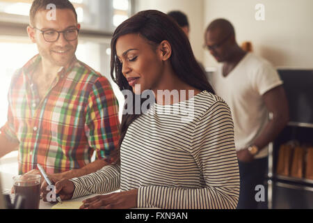 Gut aussehender Mann mit Brille und schöne Frau in gestreiften Langarm-Shirt mit Kollegen im Hintergrund am Schreibtisch arbeiten Stockfoto