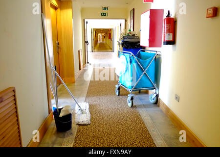 Ein Reinigungswagen des Hotels in einem Hotelkorridor vor einem Gästezimmer, der gerade gereinigt wird. Ein Wäschereiwagen wird ebenfalls vom Team benutzt Stockfoto