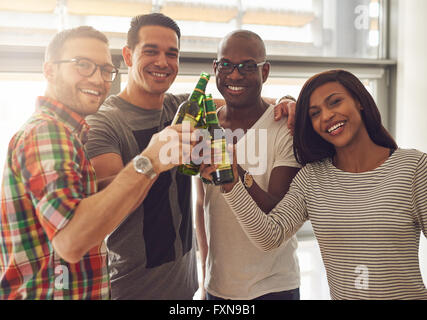 Heterogene Gruppe von vier jungen lächelnd Freunde im casual-Outfits Tippen auf grünem Glas-Bierflaschen Stockfoto