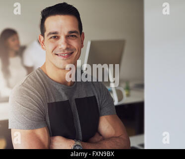 Nahaufnahme von sicher gut aussehend männlichen Arbeitnehmer mit muskulösen Arme tragen graue Kurzarm Shirt in kleinen Büro mit anderen Stockfoto
