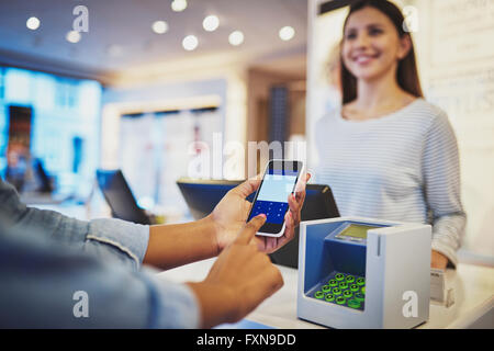 Nahaufnahme auf Finger des Kunden, die Eingabe von Informationen am Telefon vor Register als Kassiererin lächelt im store Stockfoto