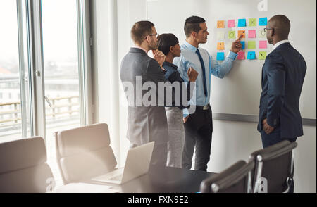 Vielfältige Gruppe von vier Menschen versammelt, um White Board mit Haftnotizen etwas Planung Stockfoto