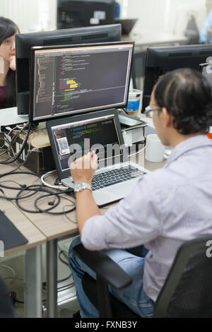 Asiatische Outsourcing Software-Entwickler suchen Bildschirm sitzen am Schreibtisch Stockfoto