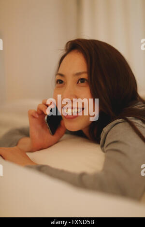 Junge attraktive Japanerin am Telefon im Bett Stockfoto