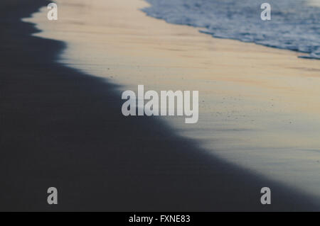 Unscharfen Hintergrund von Wellen und schwarzen Sandstrand am Sonnenuntergang Stockfoto