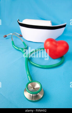 Stethoskop, Krankenschwester Hut und Herz rot Keramik auf blauem Stoff. Stockfoto