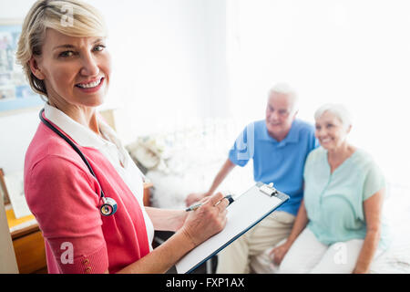 Krankenschwester auf Zwischenablage und Senior paar sitzt auf einem Bett zu schreiben Stockfoto