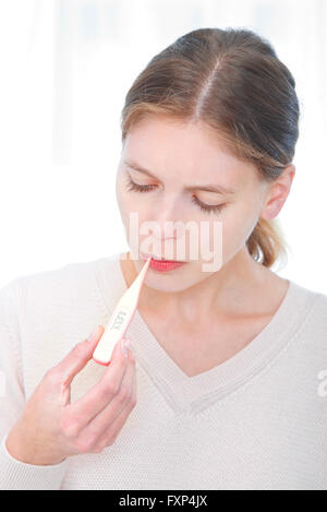 -MODELL VERÖFFENTLICHT. Junge Frau, die ihre Temperatur. Stockfoto