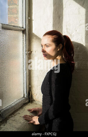 Rothaarige Frau aus dem Fenster Stockfoto