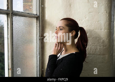 Ernste Frau, Blick aus dem Fenster Stockfoto