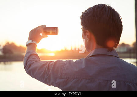 Mann fotografiert Sonnenuntergang mit smartphone Stockfoto