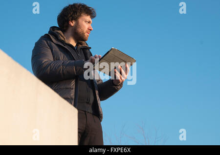 Mann hält digitale Tablet im Freien, in Gedanken wegschauen Stockfoto